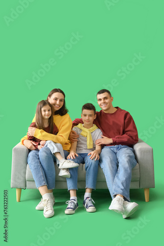 Little children with their parents sitting on sofa against green background © Pixel-Shot