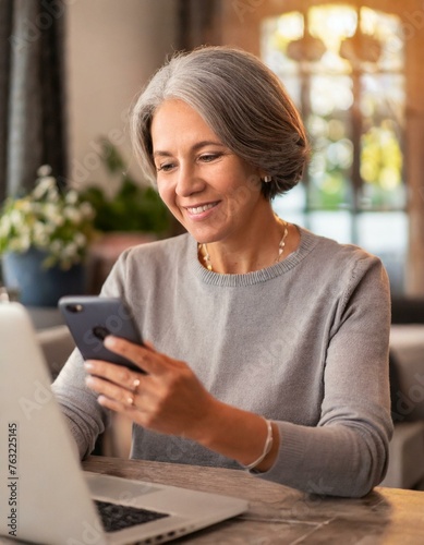 Happy smiling older woman using technology, working from home. Mature lady with a laptop and smart phone.
