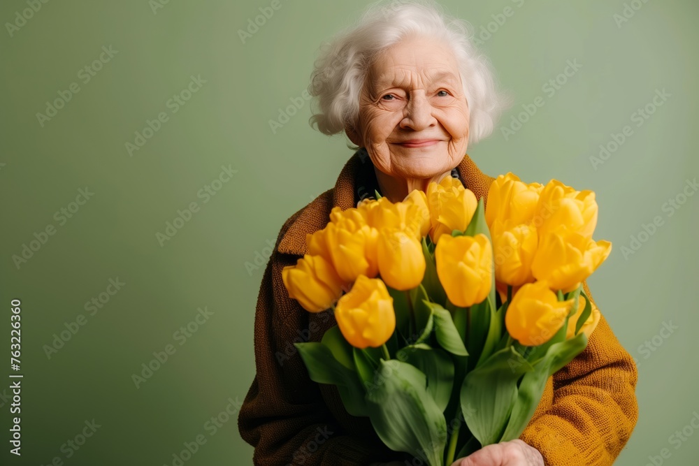 Radiant elderly woman in cardigan beams with soft smile, holding generous bouquet of yellow tulips, evoking sense of renewal, joy. Gorgeous Elderly Lady with spring flowers n olive background Radiant elderly woman in cardigan beams with soft smile, holding generous bouquet of yellow tulips, evoking sense of renewal, joy. Gorgeous Elderly Lady with spring flowers n olive background