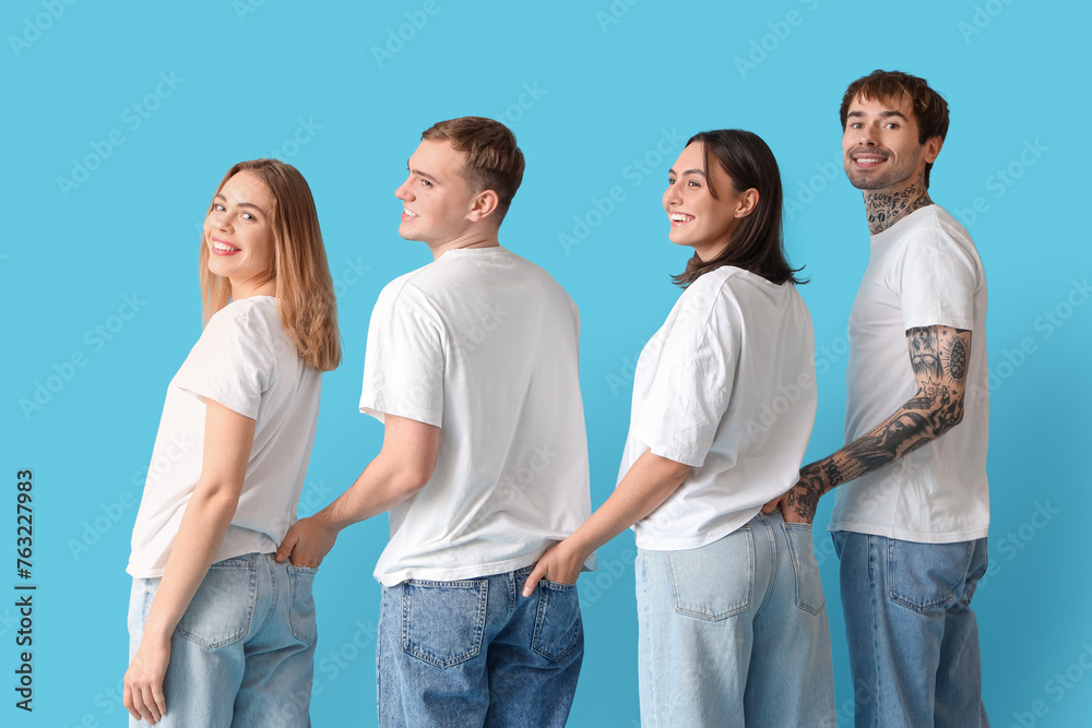 Group of young people in stylish jeans on blue background, back view