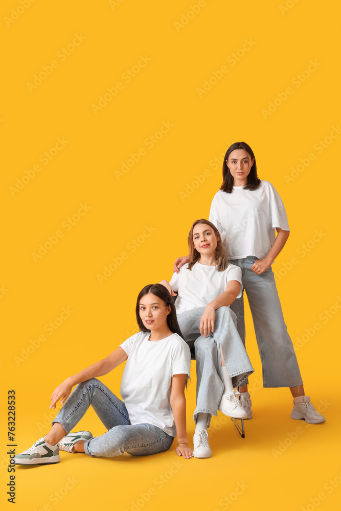 Young women in stylish jeans on yellow background