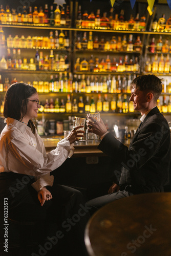 Young man and woman clinks glasses with elite drinks celebrating meeting in club. People greet each other on party in modern club