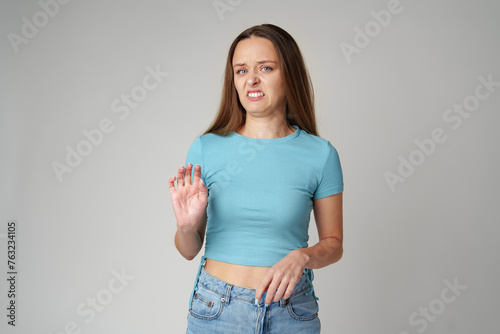 Young beautiful woman over gray background with disgusted displeased expression on gray background
