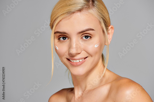 charming girl with grey eyes  perfect skin  and cream on her cheeks against grey background