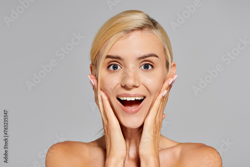 excited girl with blonde hair and gray eyes showing surprise face expression on gray background