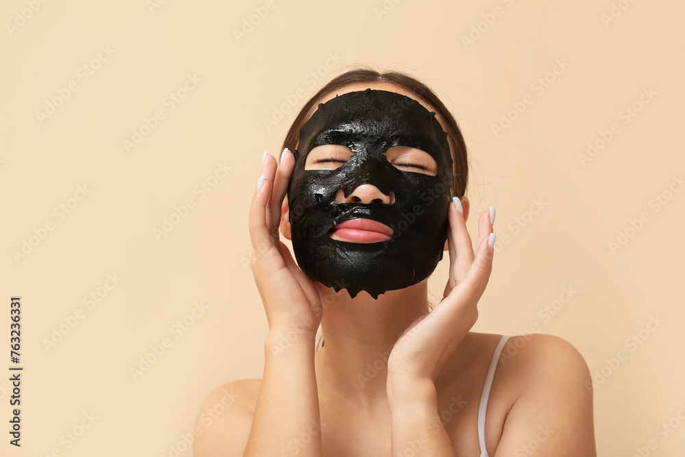 Young woman with activated charcoal mask on her face against beige background Young woman with activated charcoal mask on her face against beige background