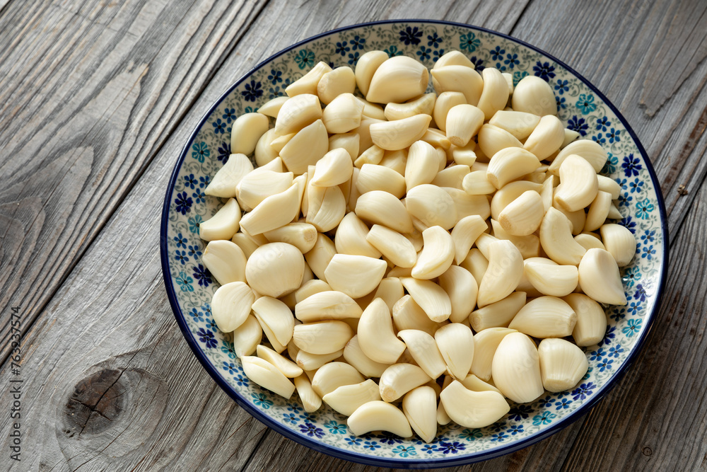 A heap of peeled garlic cloves on a plate. Naturally aged wooden table. A heap of peeled garlic cloves on a plate. Naturally aged wooden table.