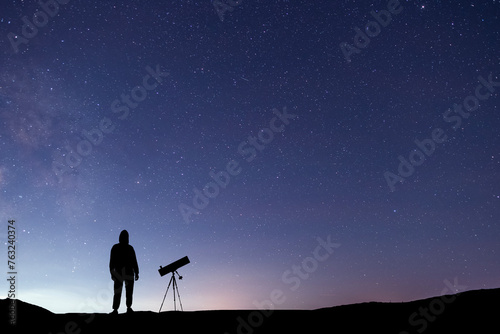 Silhouette of a hiker with telescope  standing on the hill, on the milky way galaxy background. © Inga Av