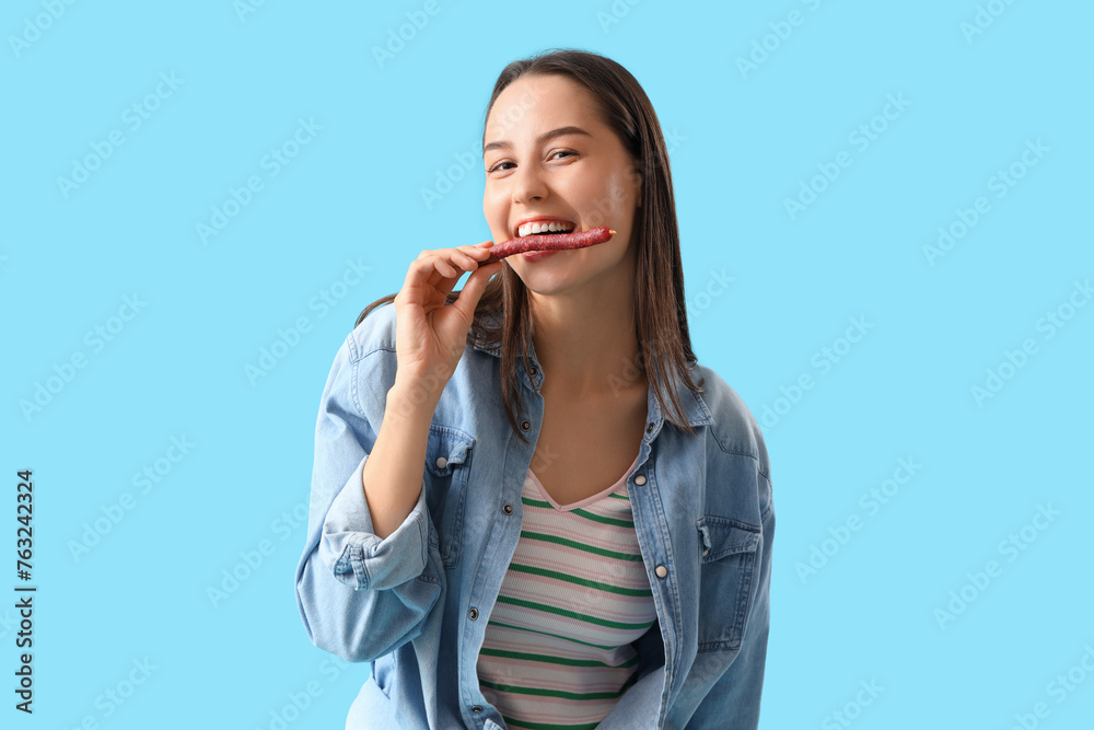 Young woman with tasty sausage on blue background Young woman with tasty sausage on blue background