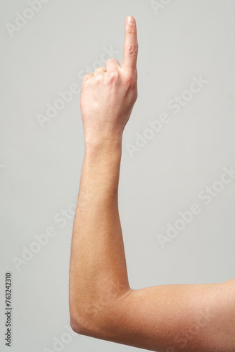 Male hand showing one finger up on gray background