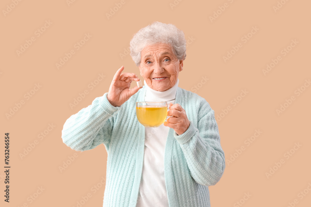 Mature woman with sugar cube and glass cup of lemon tea on beige background Mature woman with sugar cube and glass cup of lemon tea on beige background