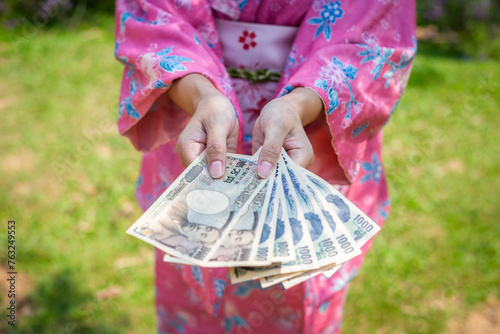 Woman wearing traditional Japanese pink kimono holding yen
