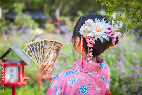 woman wearing a traditional Japanese pink kimono holds a yen in her hair decorated with flowers and beautiful accessories.