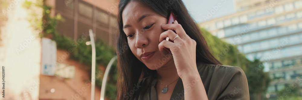 Close up, young woman talking on smartphone while sitting on modern buildings background, Panorama Close up, young woman talking on smartphone while sitting on modern buildings background, Panorama