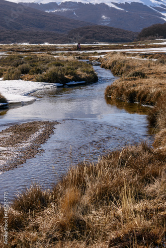 Arroyo con agua limpia, nieve y tundra en primer plano y montañas al fondo. Paisaje puro y limpio en primavera austral. Naturaleza y ecología