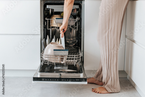 female hands turn on the dishwasher with dirty dishes in a white kitchen photo