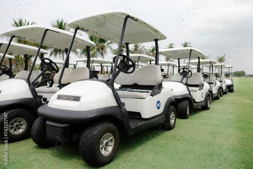Many golf carts on the golf course are ready to serve golfers.