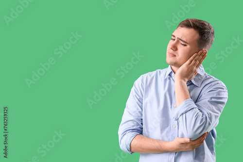 Young man suffering from ear pain on green background