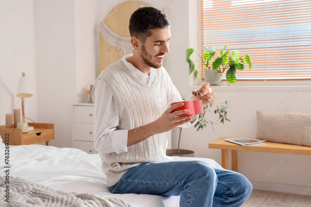 Handsome man with box of heart-shaped chocolate candies in bedroom Handsome man with box of heart-shaped chocolate candies in bedroom