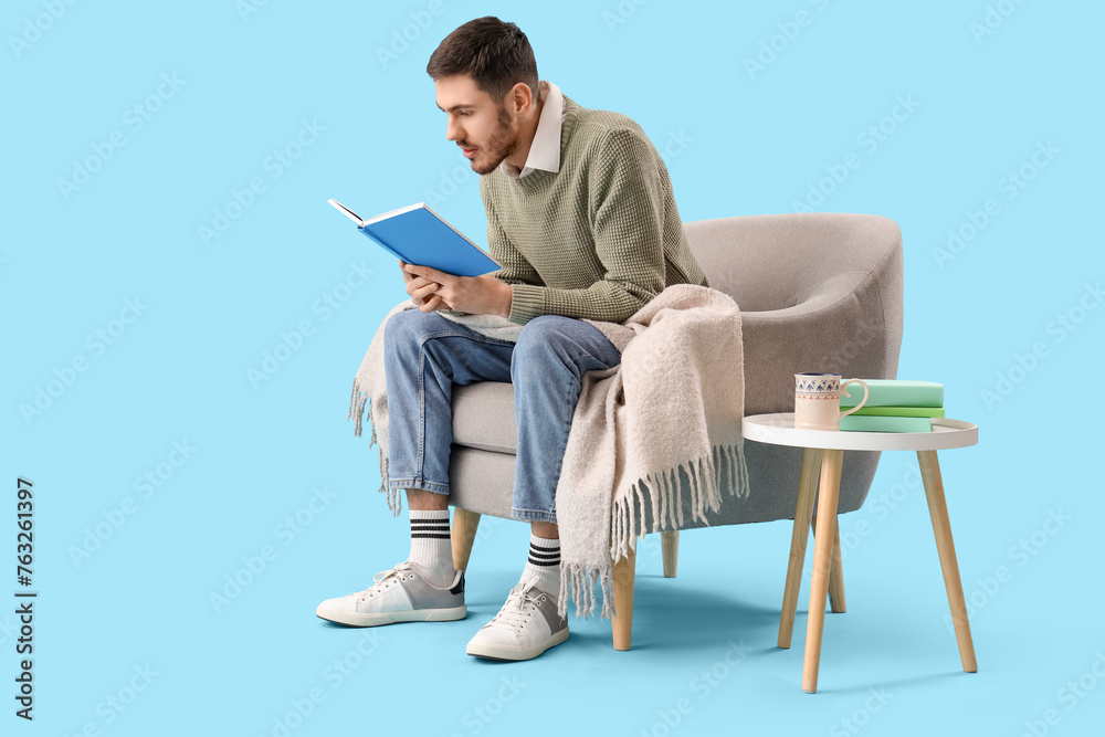 Young man reading book in armchair on blue background