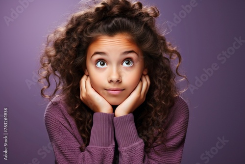 Portrait of a curious young teenage girl with long curly hair looking up and thinking, isolated on purple background, with copy space.
