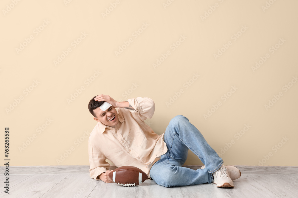 Obraz premium Young man with brain concussion and rugby ball lying near beige wall