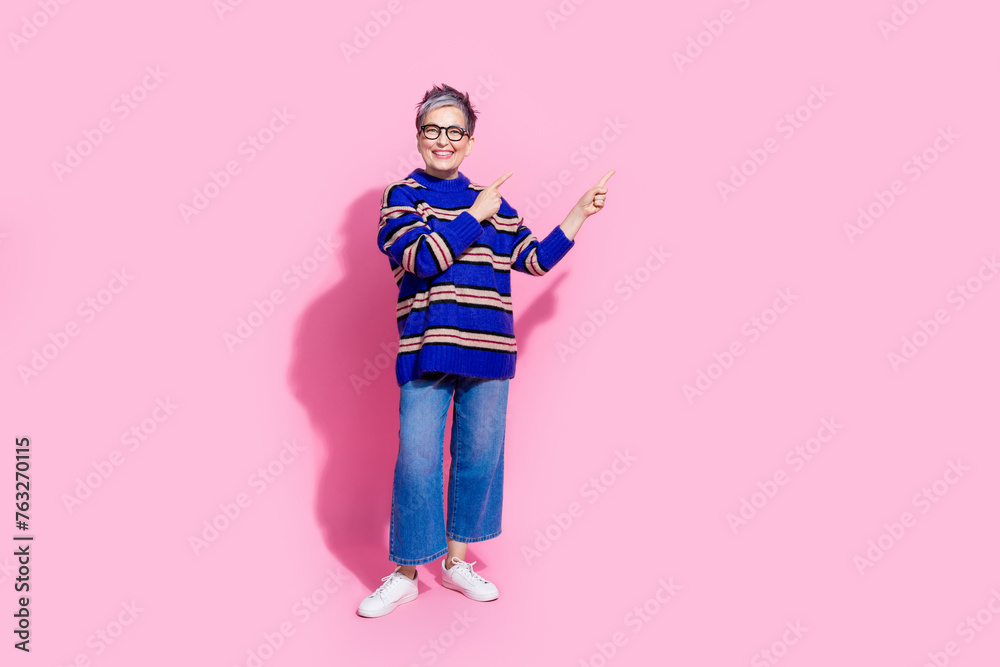 Full length photo of lovely senior lady point banner empty space wear trendy blue striped garment isolated on pink color background Full length photo of lovely senior lady point banner empty space wear trendy blue striped garment isolated on pink color background