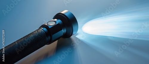 Black battery powered waterproof flashlight made of aluminum and turned on isolated on a white background.
