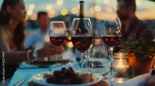 Happy people drinking red wine sitting at restaurant table - Young people of various nationalities enjoying dinner on rooftop together - Food and drink concept with man and woman having dinner photo