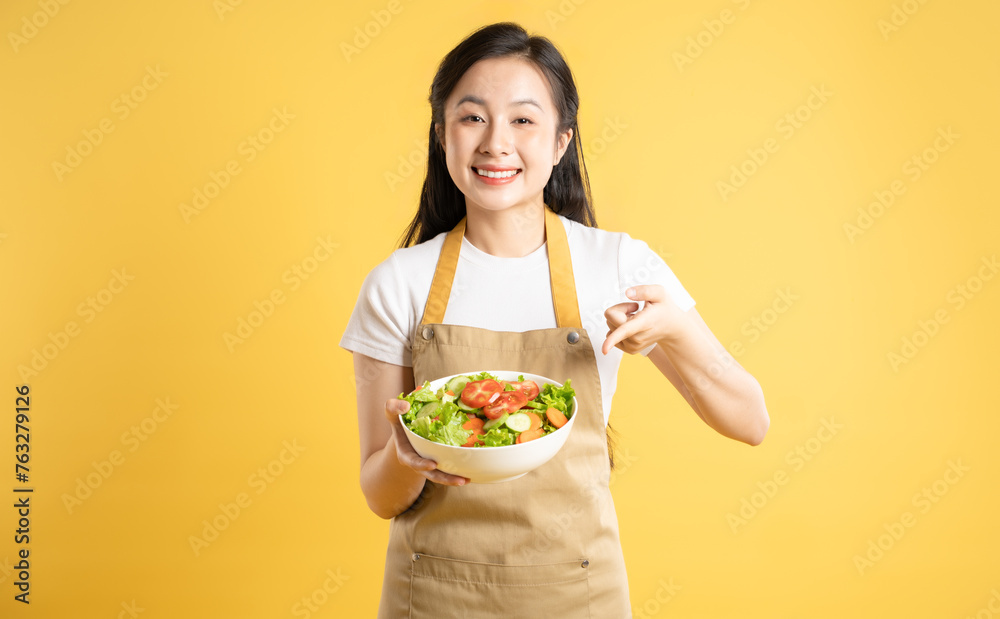 Portrait of Asian female housewife holding a bowl of salad and posing against a yellow background Portrait of Asian female housewife holding a bowl of salad and posing against a yellow background
