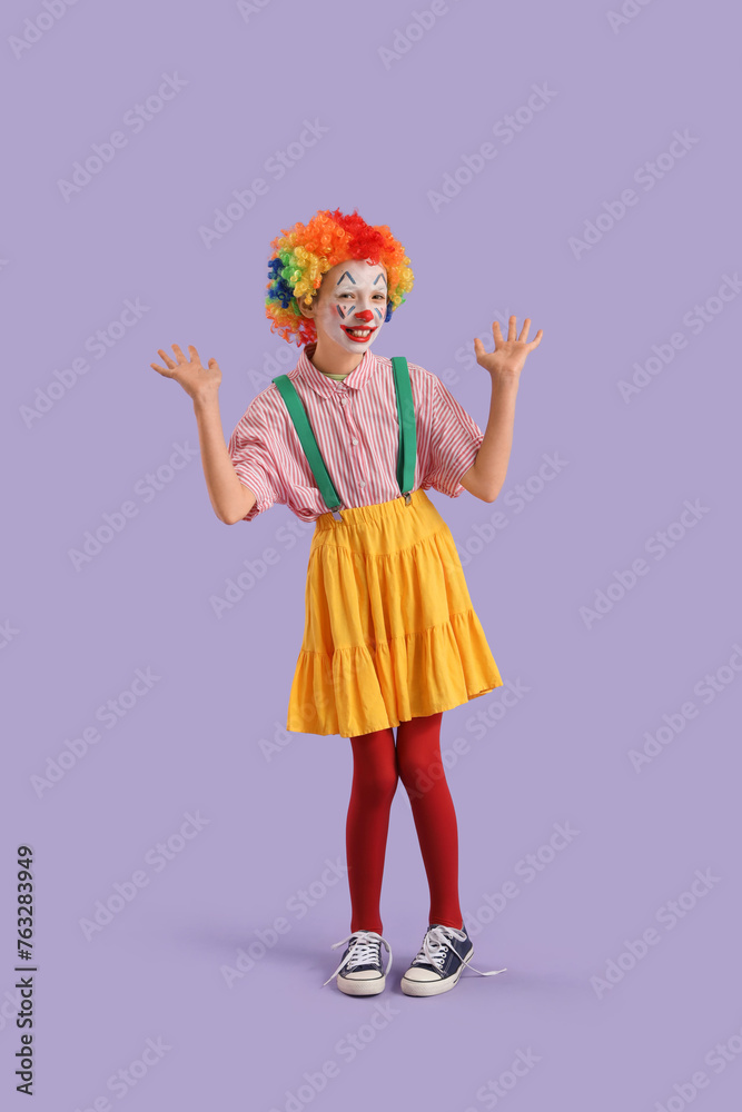 Fototapeta premium Funny little girl dressed as clown on lilac background. April Fools' Day celebration