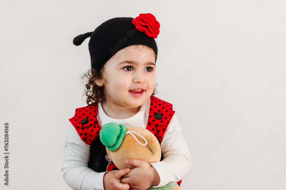 Adorable little girl in ladybug costume tenderly embracing fluffy bear against white background
