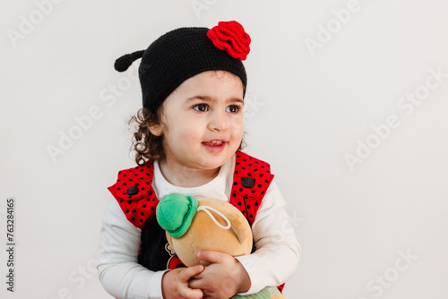 Obraz na płótnie Adorable little girl in ladybug costume tenderly embracing fluffy bear against white background w salonie