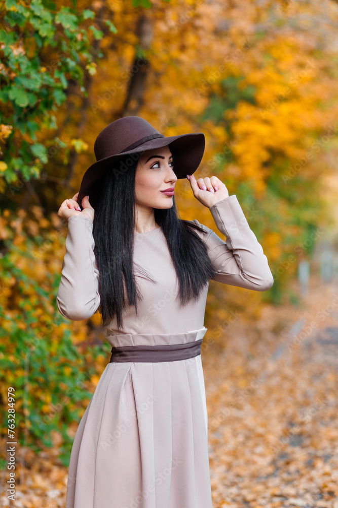Elegant young woman in wide-brimmed hat gracefully poses with poise in scenic autumn park