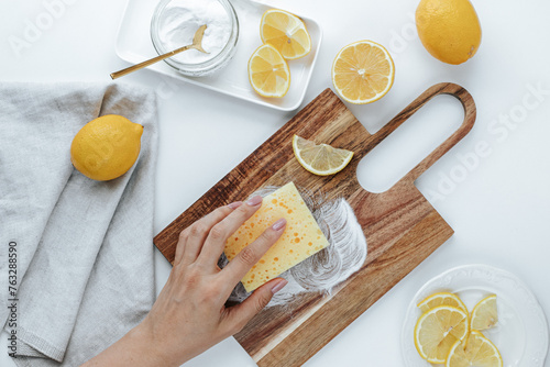 wooden cutting board with soda and lemons on a white background. a woman\'s hand with washcloths soda cleans it. rectangular plate with a can of soda and lemons