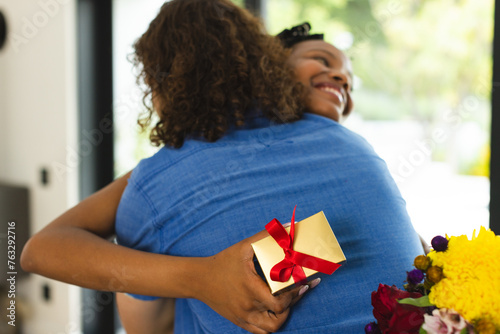 African American couple embraces warmly, woman holding gift