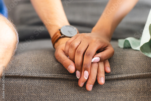 A diverse couple holds hands, showcasing unity and affection at home on the couch