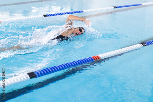 A Caucasian female athlete swimmer is swimming laps in a pool, blue background