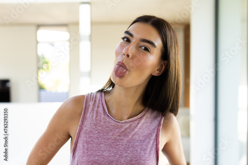 A young Caucasian brunette woman sticks her tongue out playfully at home