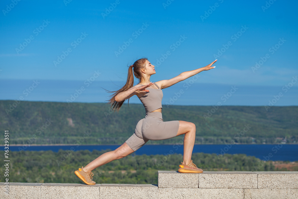 A young woman in a tracksuit performs physical exercises in a summer park A young woman in a tracksuit performs physical exercises in a summer park