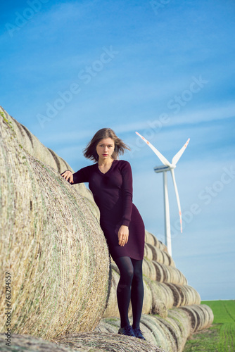 A girl with hair flying in the wind stands on a haystack