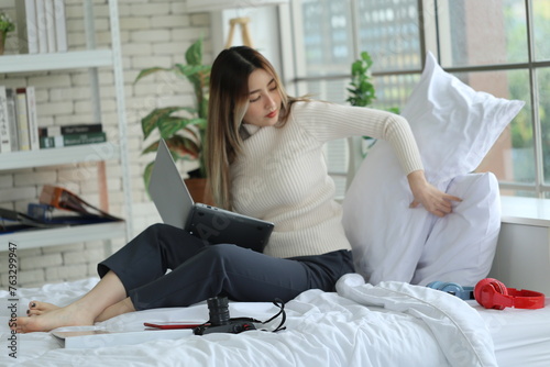 Asian woman sitting studying, doing a report on bed, working at home with laptop in apartment