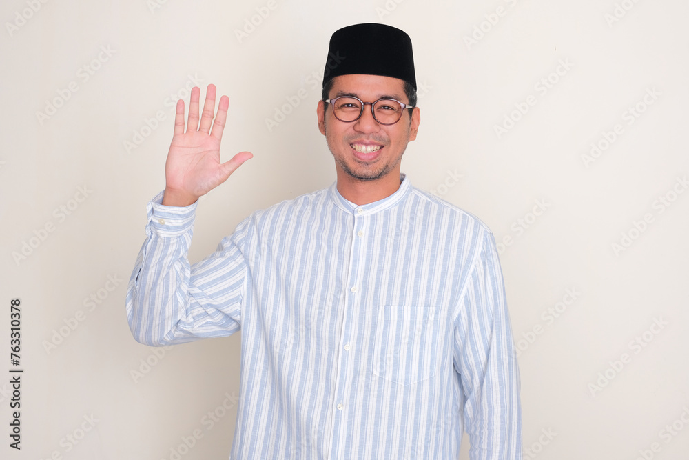 Moslem Asian man smiling happy and waving hand at the camera Moslem Asian man smiling happy and waving hand at the camera