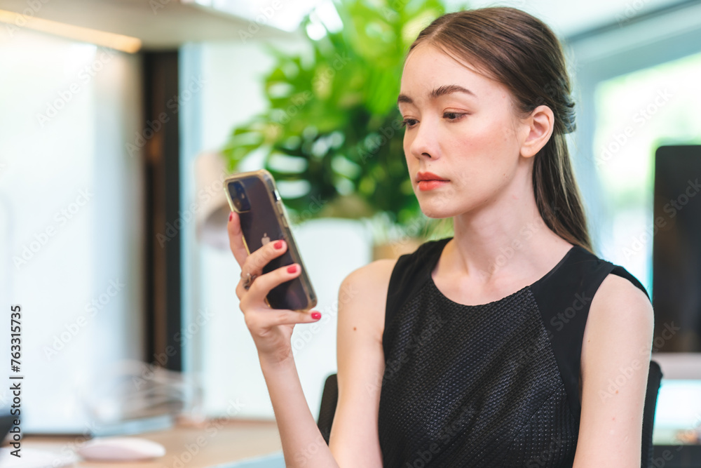 A woman is looking at her cell phone while sitting at a desk A woman is looking at her cell phone while sitting at a desk