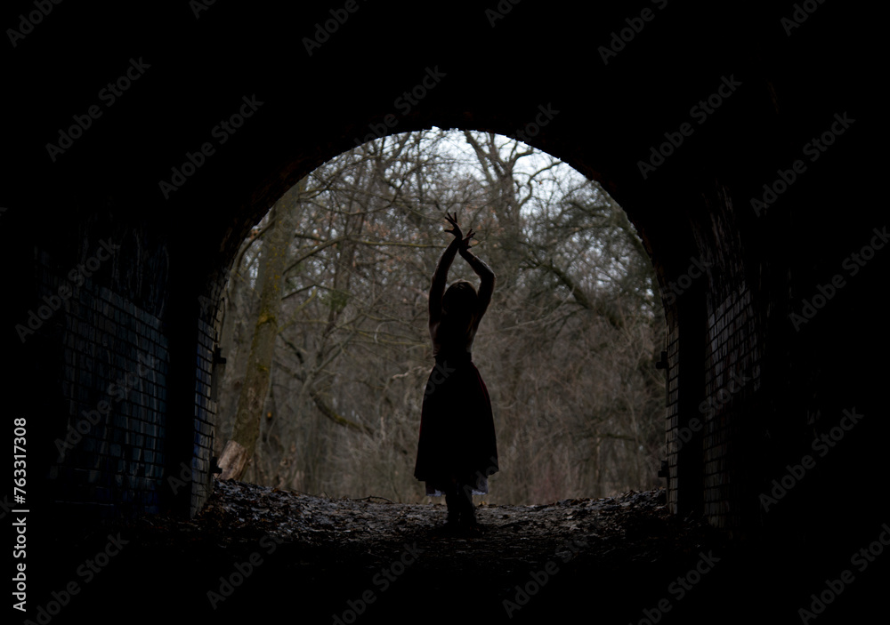 dark silhouette of dramatic lonely single woman in stone arch in winter forest - obrazy, fototapety, plakaty 