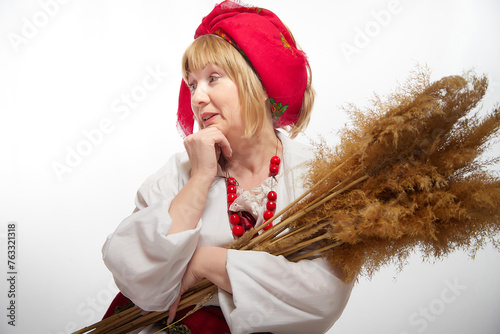 Portrait of heerful funny adult mature woman solokha with sheaf of ears. Female model in clothes of national ethnic Slavic style. Stylized Ukrainian, Belarusian or Russian woman in comic photo shoot