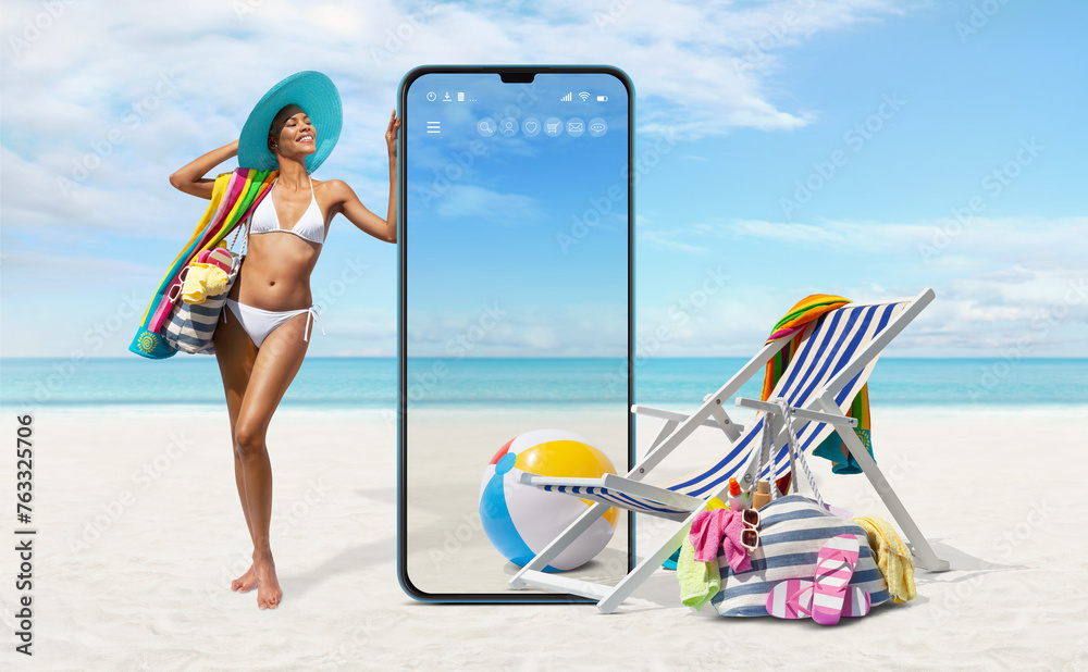 Happy girl in summer beach holiday wearing bikini showing a big screen mobile phone with deckchair and sea accessories isolated in seaside background, online shopping or booking sea vacation travels