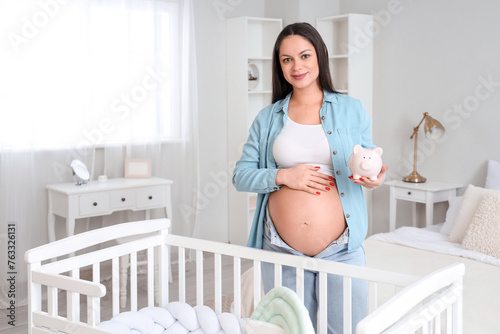 Young pregnant woman with piggy bank in children's bedroom. Maternity Benefit...