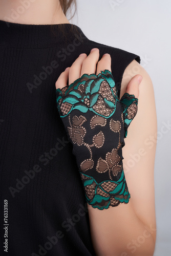 Cropped shot of a lady in a black t-shirt  and black and green lace mittens with pattern. The girl is posing on the light background. photo