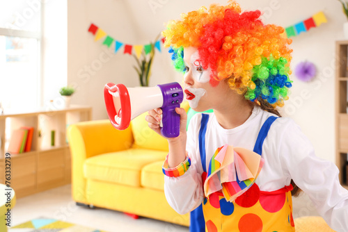 Funny little girl in clown costume with megaphone at home. April Fools' Day celebration